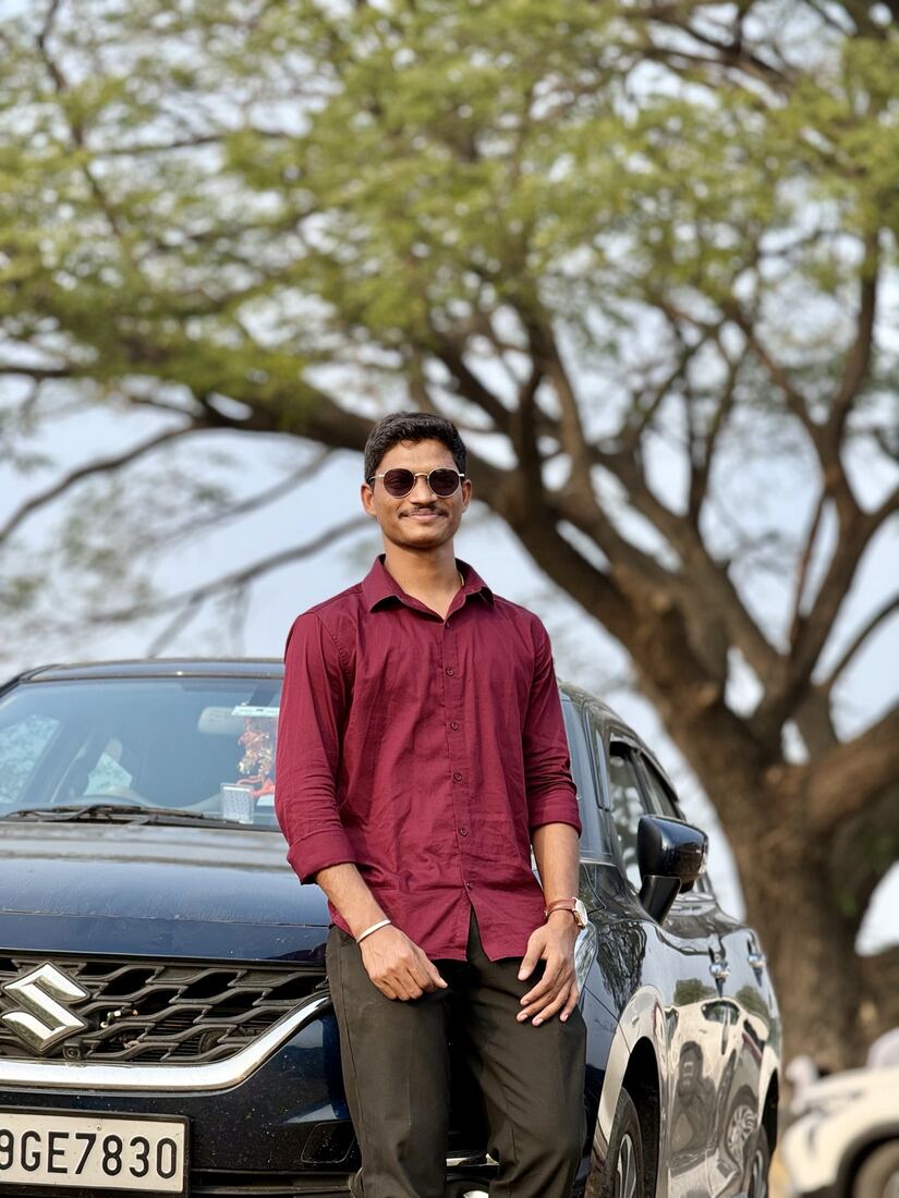 In a maroon shirt beside a car under a tree